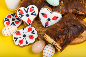 Slices of Romanian sponge cake or chec, cozonac with red traditional towel with manual stitch on wooden board, Easter painted eggs and home made ginger bread hearts, Authentic Easter Brunch concept. 