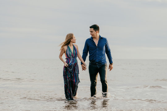 Good Looking Couple Looking Each Other Straight In The Eye, Walking Out Of The Ocean Holding Hands