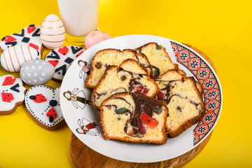 Slices of Romanian sponge cake or chec, cozonac with red traditional towel with manual stitch on wooden board, Easter painted eggs and home made ginger bread hearts, Authentic Easter Brunch concept. 