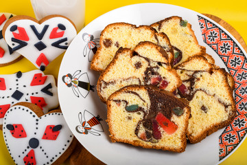 Slices of Romanian sponge cake or chec, cozonac with red traditional towel with manual stitch on wooden board, Easter painted eggs and home made ginger bread hearts, Authentic Easter Brunch concept. 