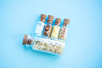 Picture with soft focus of five tiny glass jar with rice, buckwheat, millet, sugar and barley on blue background, top view. Concept of nutrition, vegetarian products. Empty copy space for text