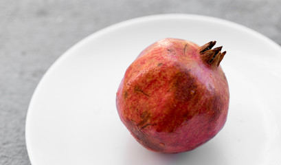 Fresh raw ripe pomegranate on a white plate, close up view, fruit, background