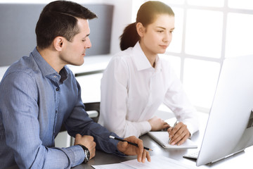 Cheerful smiling businessman and woman working with computer in modern office. Headshot at meeting or workplace. Teamwork, partnership and business concept