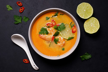 Tom Yam kung Spicy Thai soup with shrimp, coconut milk and chili pepper in bowl. Black stone background