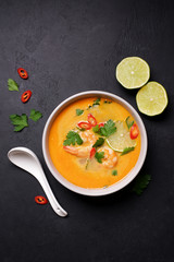Tom Yam kung Spicy Thai soup with shrimp, coconut milk and chili pepper in bowl. Black stone...