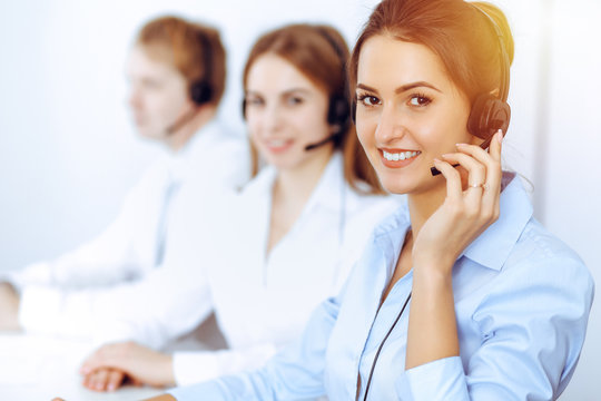 Call center operators. Focus on beautiful business woman using headset in sunny office