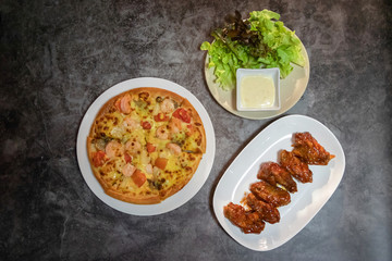 Pizza seafood with prawn and tomato, deep fried chicken wing with spicy sauce in Korean style and salad on table. Top view