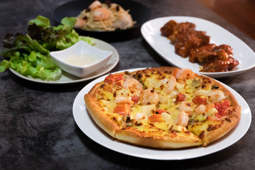 Pizza seafood with prawn and tomato, deep fried chicken wing with spicy sauce in Korean style, salad and spaghetti on table. 