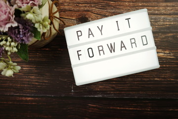 Pay It Forward word in light box with space copy on wooden background