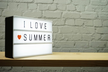 I Love Summer word in light box on white brick wall and wooden background