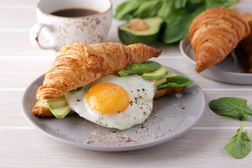 Croissant avocado toast with spinach and fried eggs. Healthy breakfast in plate on light wooden table