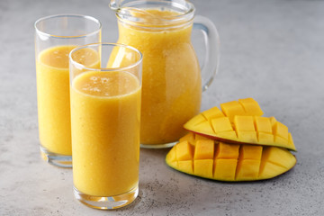 Mango and oranges smoothie. Fresh drink pouring into glass from glass jur