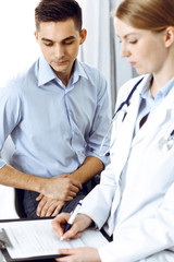 Female doctor holding application form while consulting man patient in hospital office. Medicine and healthcare concept