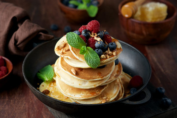 Pancakes decorated with raspberries, blueberries, mint and honey. Homemade fritters for breakfast in pan