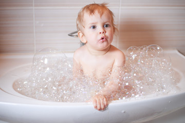 Funny child playing with water and foam in a bathroom.