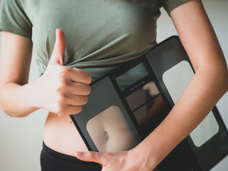 Slim Woman holds weight scale and shows thumb up. People, sport, fitness concept