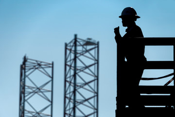 Silhouette of a Barge Foreman giving instruction on a walkie-talkie to team of roughneck at an oil...