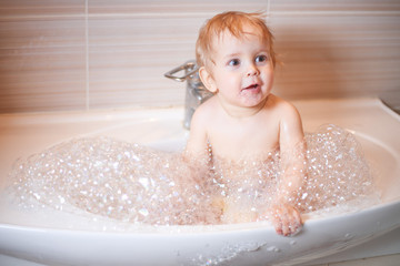 Happy laughing Infant baby toddler taking a bath playing with foam bubbles. Children care and hygiene concept.