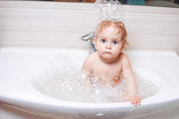Funny child playing with water and foam in a bathroom.