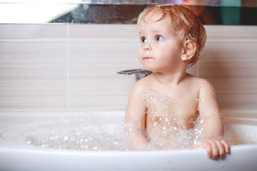 Funny child playing with water and foam in a bathroom.