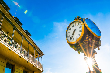 Old golden vintage clock with greek numbers, sunflare, building and blue sky in the background. Old...