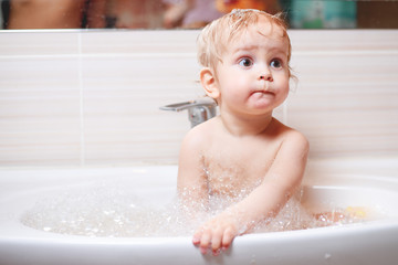 Funny child playing with water and foam in a bathroom.