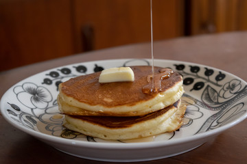 自宅で手作りしたパンケーキ　お皿に盛り付けたパンケーキにメープルシロップをかける様子