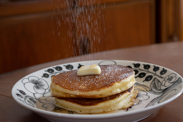 自宅のホットプレートで焼いたパンケーキ　仕上げに粉砂糖をふりかける様子