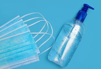 Fototapeta na wymiar Surgical face masks and disinfectant gel against blue background