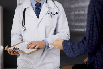 Unknown red-bearded doctor and patient woman discussing current health examination while sitting in...