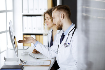 Red-bearded doctor with female colleague discussing current disease therapy while sitting at...