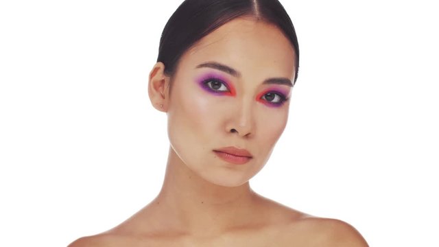 A calm half naked asian woman with bright fashion eye makeup is posing and looking to the camera isolated over white background in studio