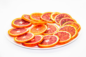 Naklejka na ściany i meble Sicilian sliced ​​orange on a white plate on a white background. Sliced ripe Sicilian oranges against background. Healthy and tasty red sliced ​​orange