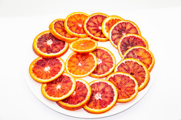 Naklejka na ściany i meble Sicilian sliced ​​orange on a white plate on a white background. Sliced ripe Sicilian oranges against background. Healthy and tasty red sliced ​​orange