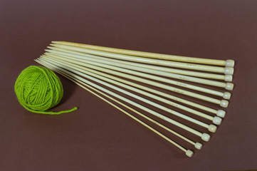 One small ball of green wool yarn and a set of knitting needles fan-shaped on a brown background. The choice of knitting needles. Hobbies, homework, needlework. Natural colors and materials. Close-up.