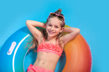 Little girl dressed in a swimsuit lying on an inflatable color ring on yellow background.