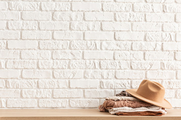 Fototapeta na wymiar women's casual outfits and brown trendy hat on wooden table over white brick wall. Minimalistic concept of home decor. Template.