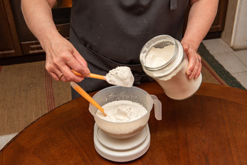 a woman puts flour in a bowl on a kitchen scale to prepare homemade dough. Cooking at home