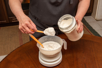 Fototapeta na wymiar a woman puts flour in a bowl on a kitchen scale to prepare homemade dough. Cooking at home