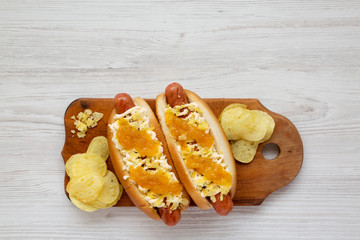 Homemade colombian hot dogs with pineapple sauce, chips and mayo ketchup on a rustic wooden board on a white wooden surface, top view. Overhead, flat lay, from above. Space for text.