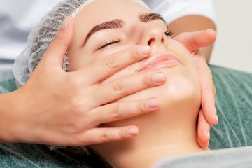 Young woman receiving head massage by hands of cosmetologist in beauty salon, close-up.