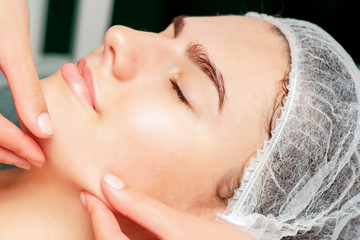 Fingers of cosmetologist checking skin face of young woman before the liposuction procedure.