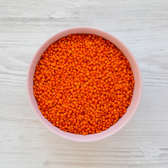 Red lentils in a pink bowl on a white wooden table, top view. Flat lay, overhead, from above.
