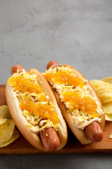 Homemade colombian hot dogs with pineapple sauce, chips and mayo ketchup on a rustic wooden board on a gray background, low angle view. Copy space.