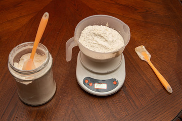 flour in a cup on a table and in a bowl on a kitchen scale. home kitchen