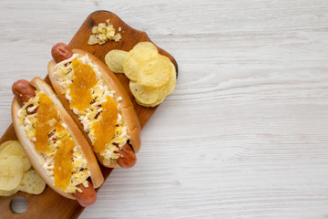 Homemade colombian hot dogs with pineapple sauce, chips and mayo ketchup on a rustic wooden board on a white wooden background, top view. Overhead, flat lay, from above. Copy space.