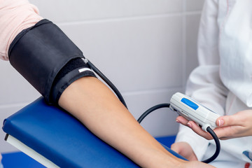 Nurse is measuring the pressure on arm of woman in the hospital.