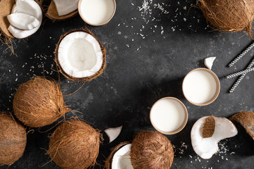 Coconut milk, whole and cracked coconuts on black background, top view