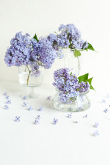 Fresh lilac flowers in a glass vase on the white table. Spring concept.