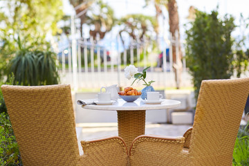 Morning coffee with fresh pastries and news a newspaper in the fresh air. A plate of pastries, coffee and cream are on the table decorated with a vase with a white rose with space for text
